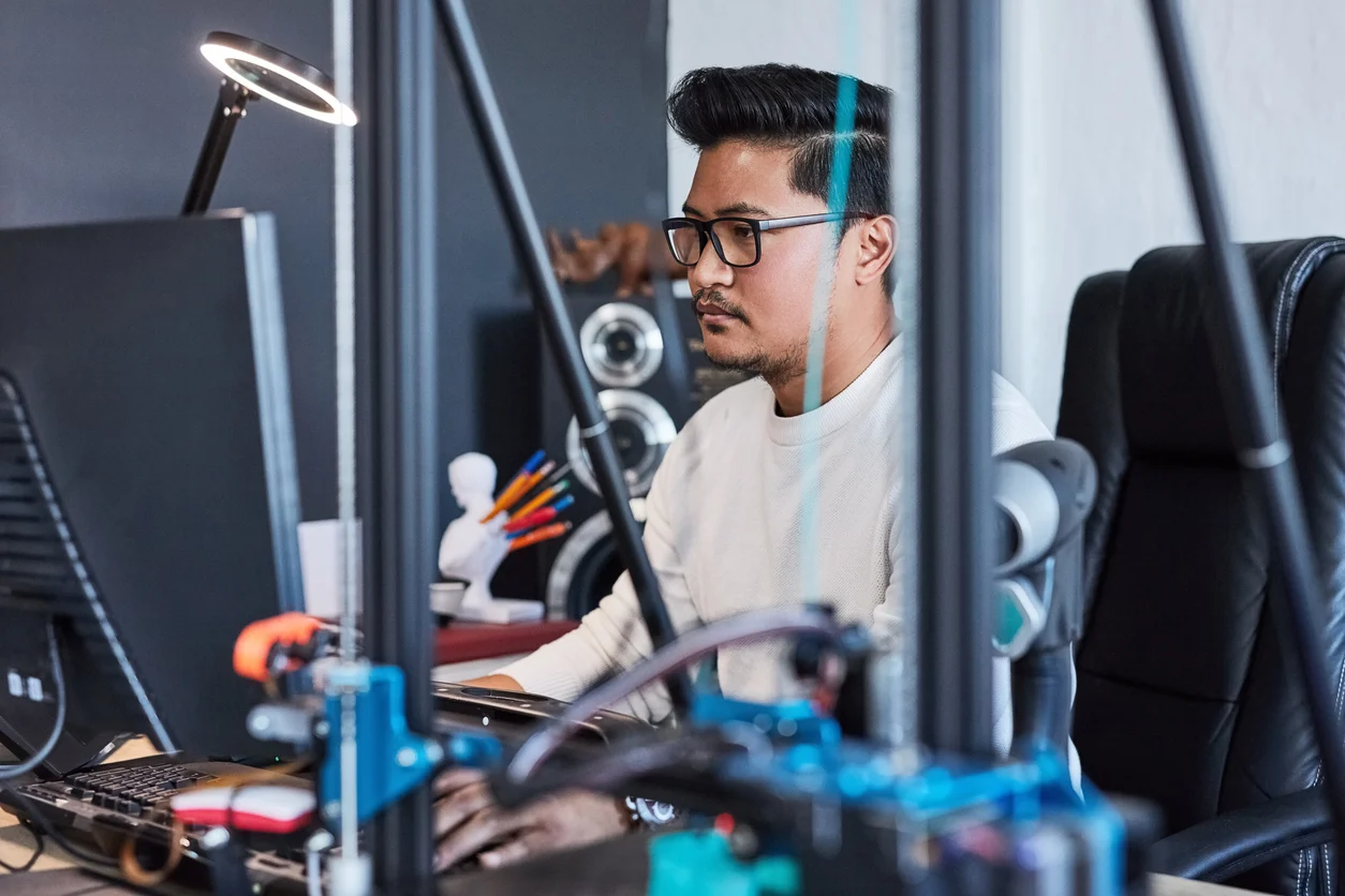 Man at computer with project for 3d printer, tech and futuristic design process tools in office. Engineering workshop, technology developer or designer at desk with machine for model manufacturing.